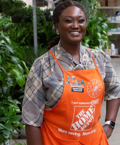 An Assistant Store Manager stands in an aisle of plants looking at the camera.